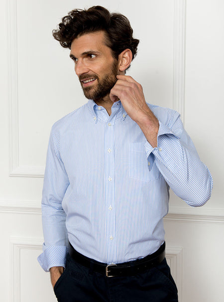 Man wearing long sleeved shirt with sky blue and white thin stripe and the inside collar and cuffs trimmed with gingham pattern. Made with 100% cotton in Thomas Mason fabric.